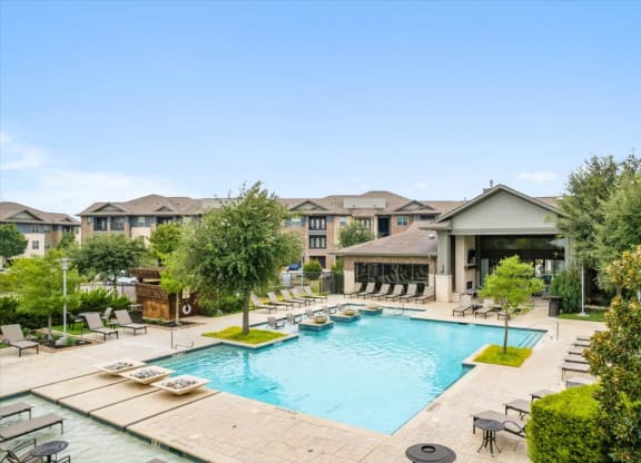 a swimming pool with chaise lounge chairs and trees in front of a building