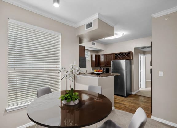 a dining area with a table and chairs and a kitchen in the background at The Clairborne Apartment Homes, Grand Prairie, TX