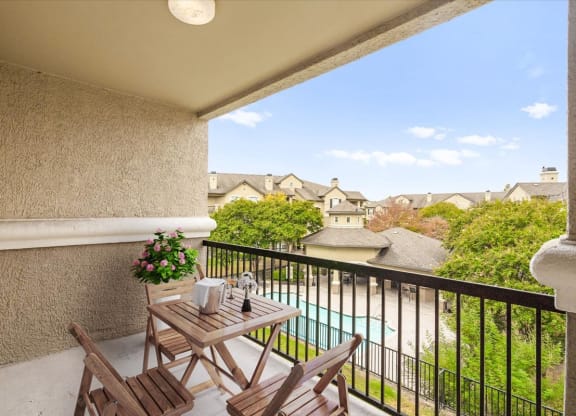 a balcony with a table and chairs and a pool in the background
