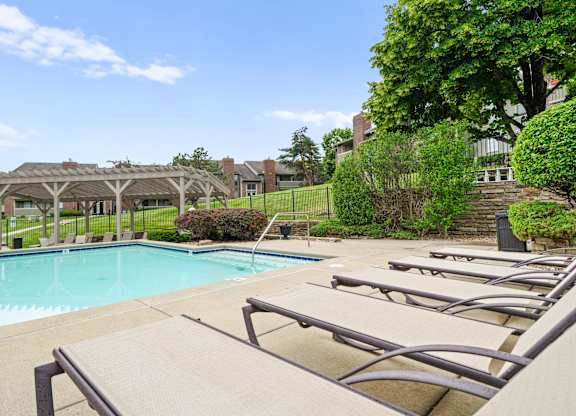 A pool with sun loungers and a pavilion in the background.