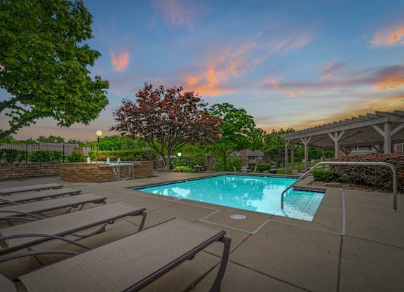 A pool surrounded by trees and lounge chairs.