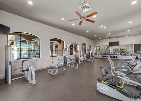 a gym with various exercise machines and a ceiling fan