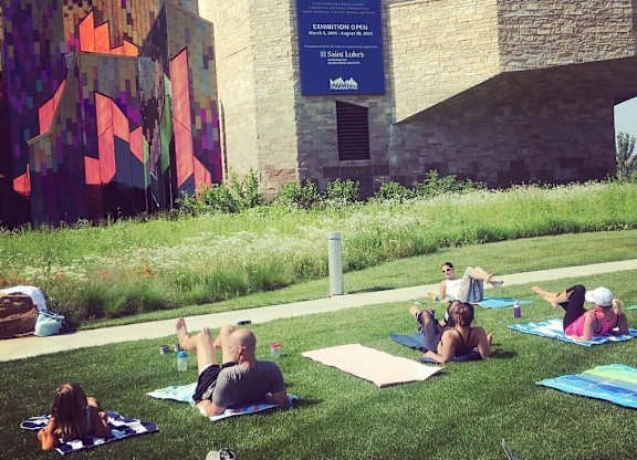 A group of people are sitting on the grass in front of a building with a large poster of a brain on it. at Residences at Prairiefire Apartment Homes, Overland Park, Kansas