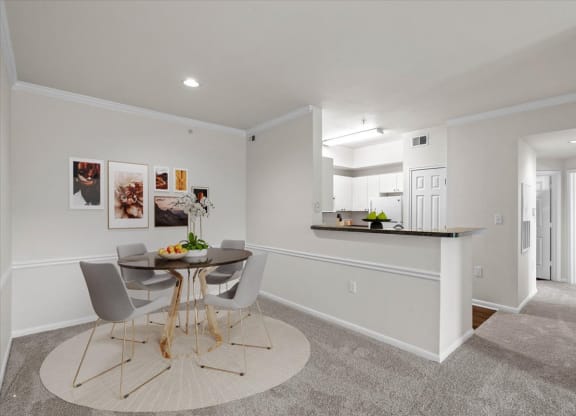 a dining area with a small table and chairs and a kitchen in the background