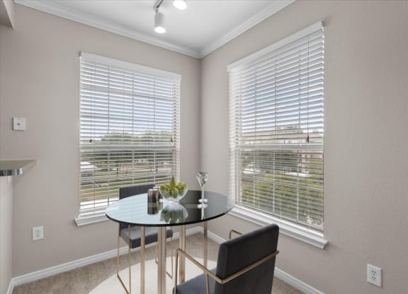 a dining room with two windows and a table with two chairs at The Clairborne Apartment Homes, Grand Prairie, Texas