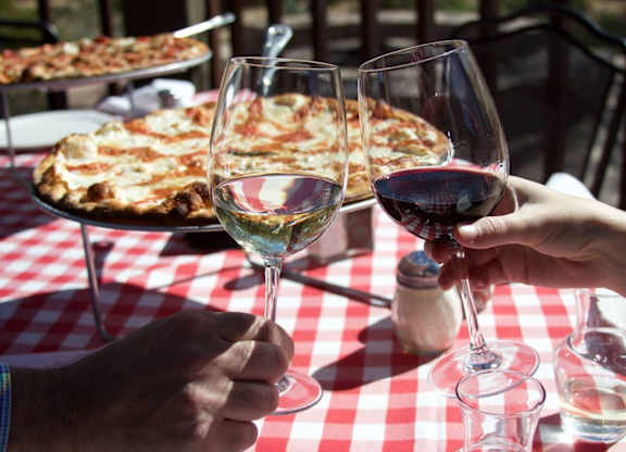 Two people toasting with wine glasses in front of a pizza. at Residences at Prairiefire Apartment Homes, Overland Park, 66223