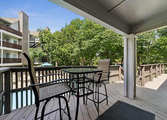 A wooden deck with a table and chairs overlooking a pool.