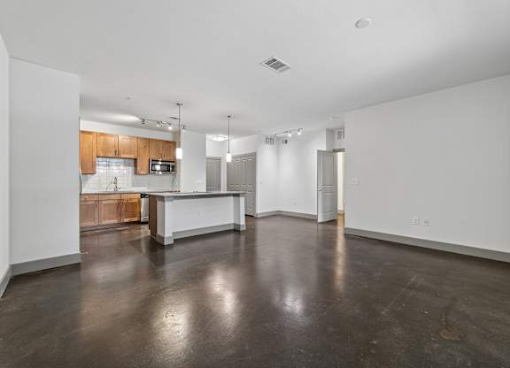 A large empty room with a kitchen area in the background.