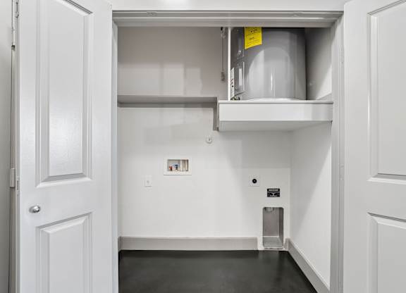 A white door is open to a small storage room with a shelf and a container.