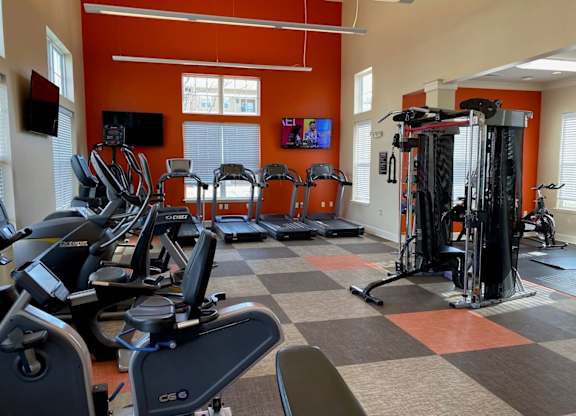 A gym with orange walls and a variety of exercise equipment. at Residences at Prairiefire Apartment Homes, Overland Park, KS, 66223