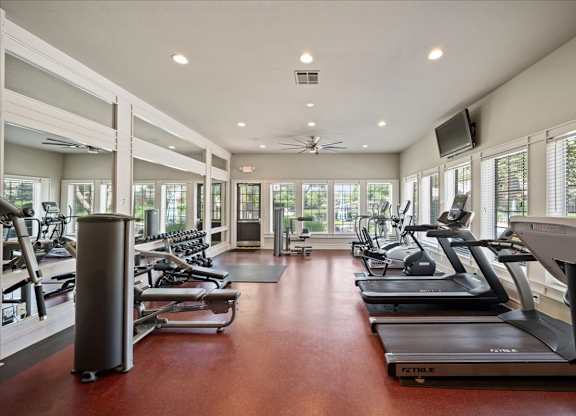 A gym with treadmills, exercise bikes, and a television.