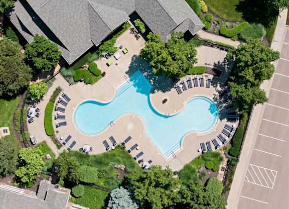 An aerial view of a swimming pool surrounded by trees and a parking lot.