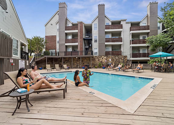 A group of people are relaxing by a pool in front of a large apartment building.