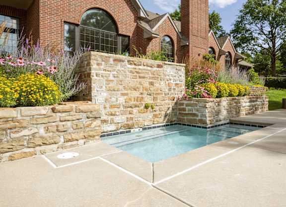 Shallow kiddie pool with stone landscaping and flower beds beside the community pool area.