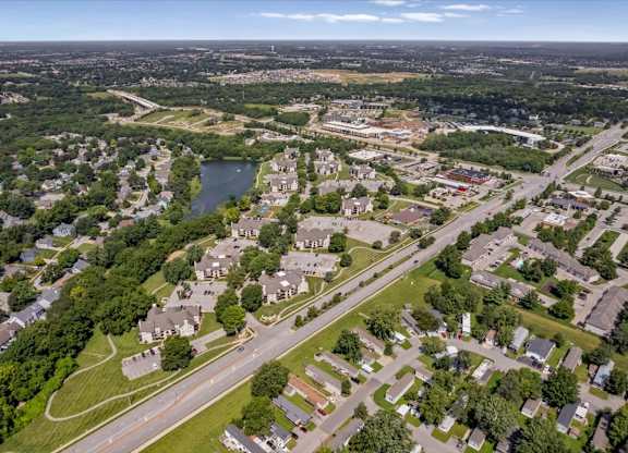 Elevated drone view of Millcreek Woods Apartment Homes in Olathe, Kansas, showcasing residential buildings, surrounding neighborhoods, mature trees, and nearby roadways.