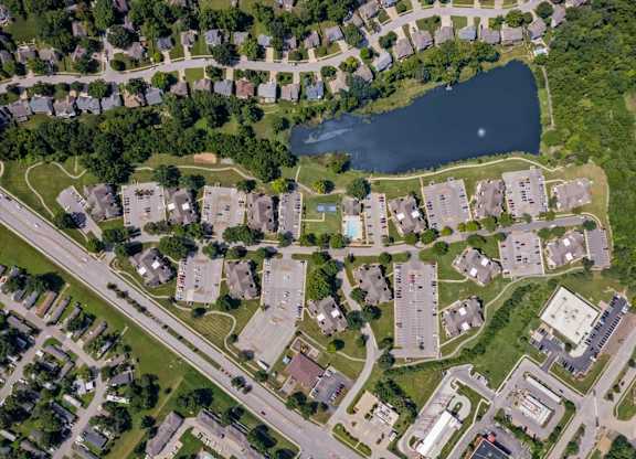 Top-down aerial view of Millcreek Woods Apartment Homes featuring apartment buildings, parking areas, landscaped grounds, and the community lake.