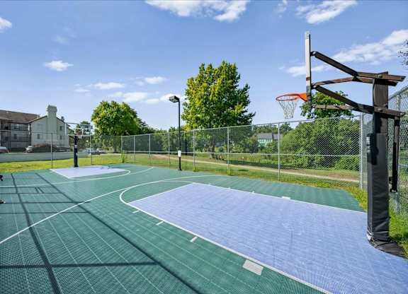 Fenced outdoor basketball court with a well-maintained playing surface at Millcreek Woods Apartment Homes.