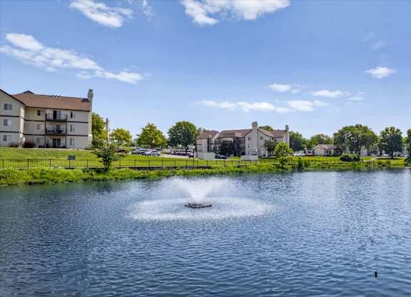 Scenic lake with decorative fountain, waterfront apartment homes, and landscaped shoreline.