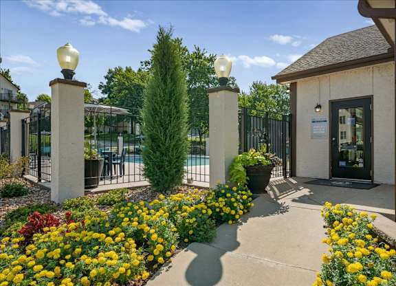 Welcoming leasing office entrance with landscaped flower beds and nearby community pool views.