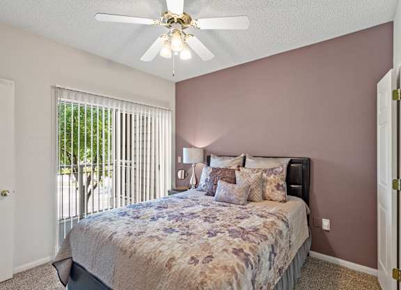 A bedroom with a ceiling fan and sliding glass door patio.