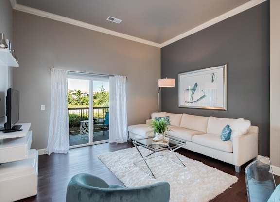 A living room with a white couch, a glass coffee table, and a painting on the wall at Residences at Prairiefire Apartment Homes, Kansas, 66223