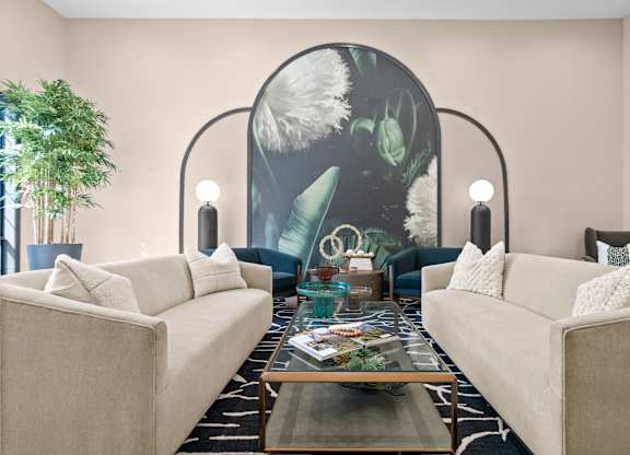 A living room with two beige couches, a glass coffee table, and a large mural on the wall.