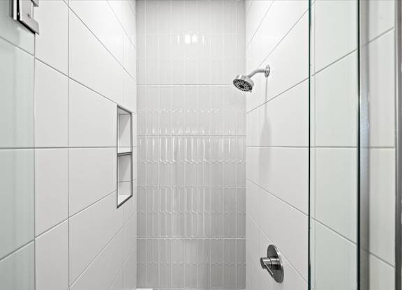 A white tiled shower with a glass door and a silver handle.