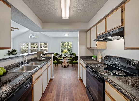 Apartment kitchen with black appliances, double sink, and open dining area at Stonebriar Apartments