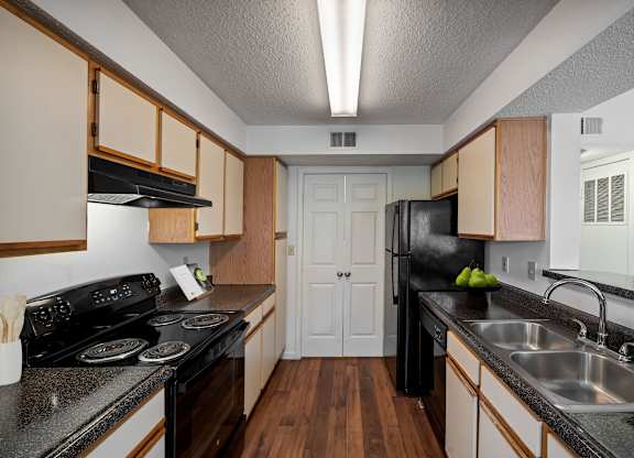 Galley-style kitchen with wood cabinets and black appliances at Stonebriar Apartments Overland Park