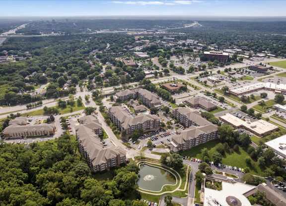 Aerial view of The Claremont Apartments community showcasing residential buildings, a scenic pond, and nearby Overland Park, Kansas neighborhoods.