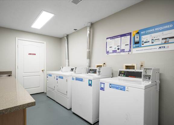 Resident laundry facility at The Claremont Apartments in Overland Park, KS, featuring multiple coinless washers and dryers, folding counters, and bright interior lighting.