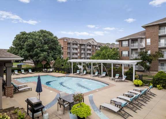 Resort-style outdoor swimming pool at The Claremont Apartments with lounge seating, shaded areas, and surrounding apartments in Overland Park, KS.
