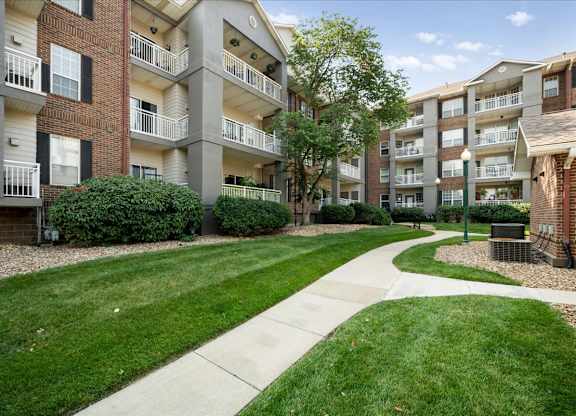 Landscaped pedestrian walkway between apartment buildings at The Claremont Apartments featuring manicured lawns and mature trees in Overland Park, KS.