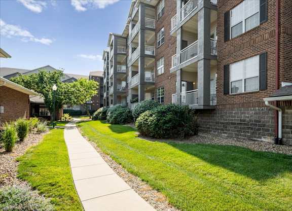 Sidewalk and green space alongside apartment buildings with private balconies and professional landscaping at The Claremont Apartments in Overland Park, KS.