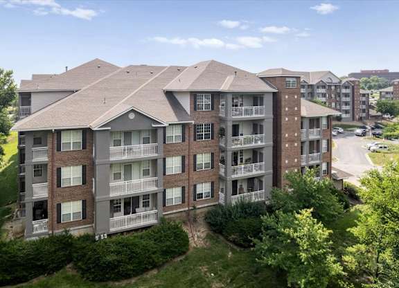 Exterior view of a residential apartment building with private balconies and mature landscaping at The Claremont Apartments in Overland Park, KS.