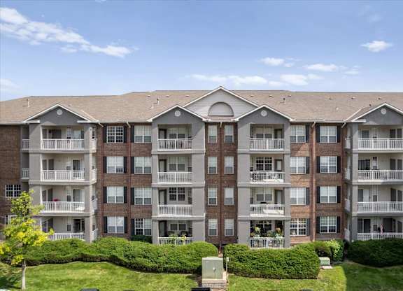 Multi-story apartment building exterior featuring private balconies, landscaped green space, and well-maintained grounds at The Claremont Apartments in Overland Park, KS.