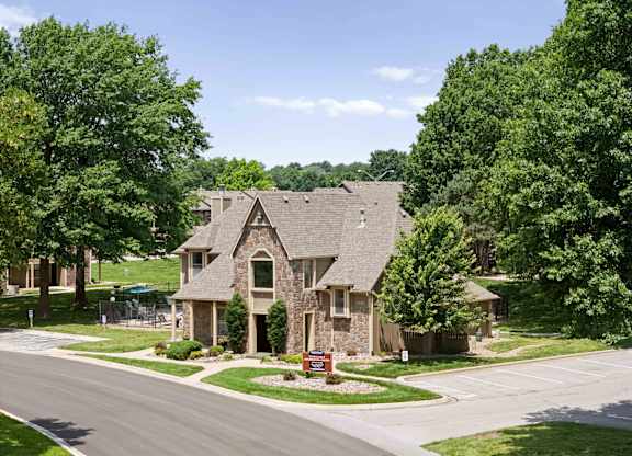 A house with a stone facade is surrounded by green trees.