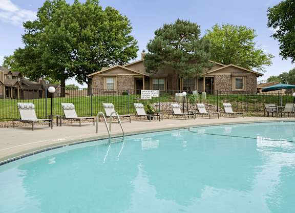 A pool with chairs around it and houses in the background.