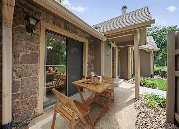 A wooden table and chairs are on a patio outside a house.