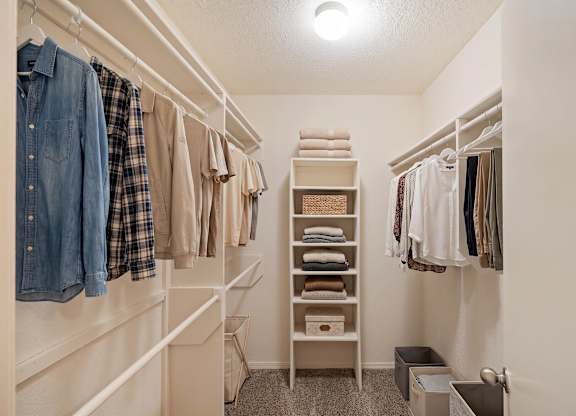 A white closet with clothes hanging and shelves with folded clothes.