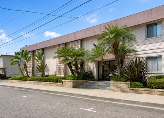 A building with a white wall and a brown roof with a tree in front of it.