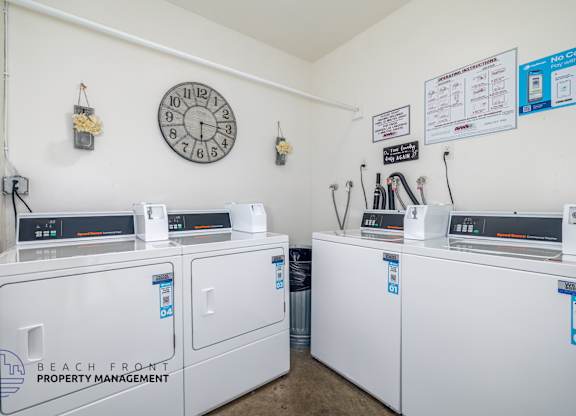 A laundromat with a clock on the wall and machines with stickers on them.