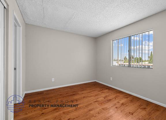 A room with wooden flooring and a window showing a view of trees and a building.