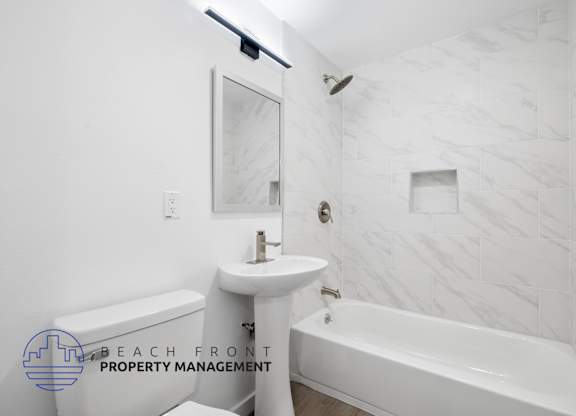 A white bathroom with a marble tile wall and a bathtub.