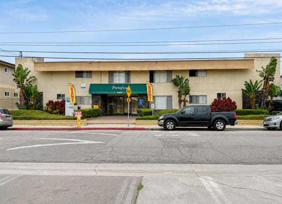 A building with a green awning and a sign that says "The Woodlands" is in front of a street with cars parked on the side.