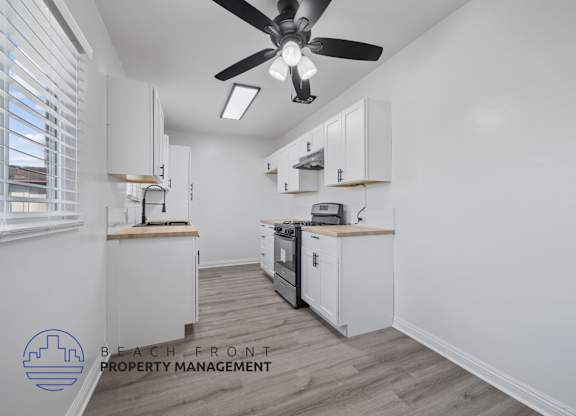 A kitchen with a ceiling fan and wooden flooring.