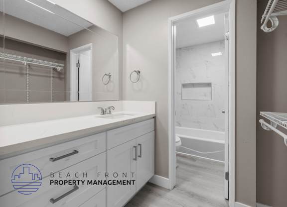 A bathroom with a sink, mirror, and a logo for Beach Front Property Management.