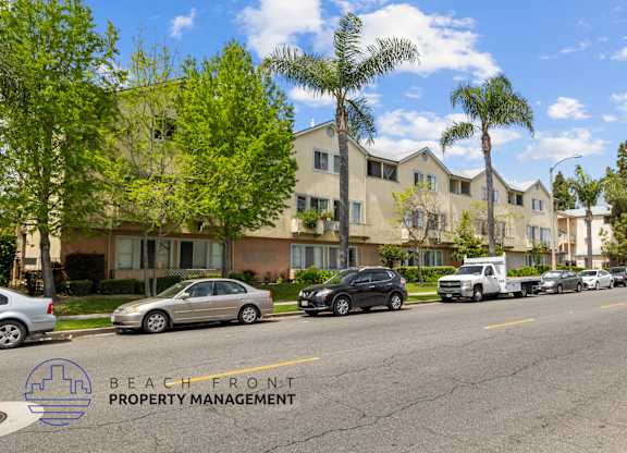 A street view of a residential area with cars parked on the side of the road and apartment buildings in the background.