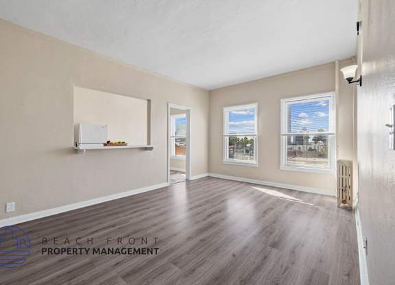 A spacious room with wooden flooring and a view of K-town through the windows.