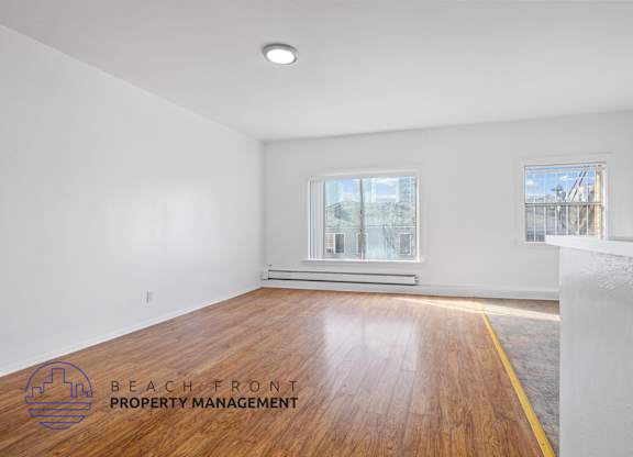A room with wooden flooring and two windows, one of which has a view of a construction site.